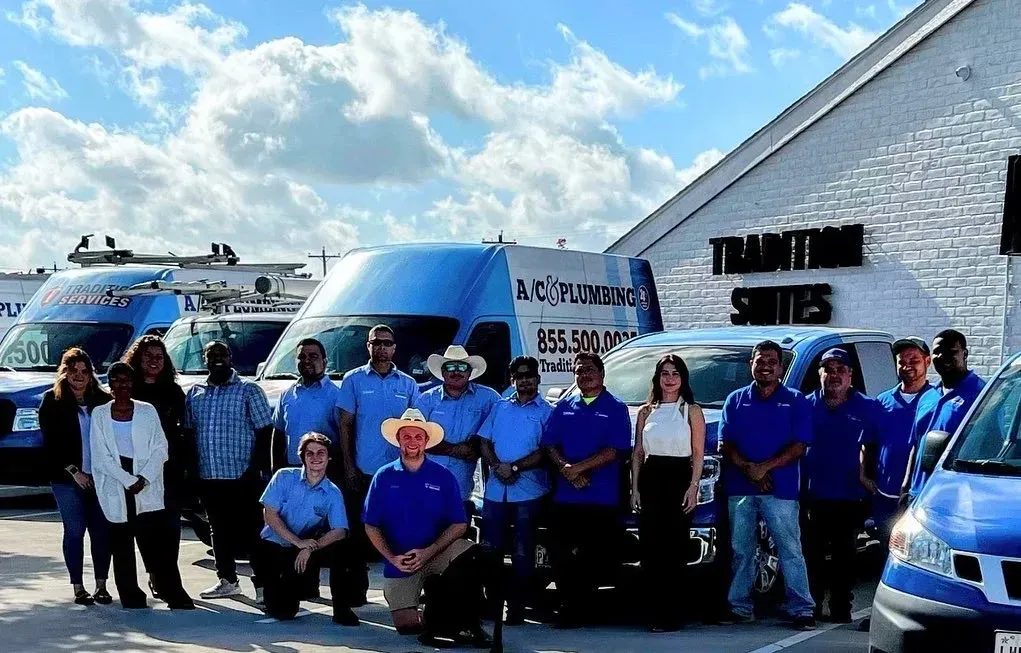 Team of plumbing professionals posing in front of service vehicles and a building.